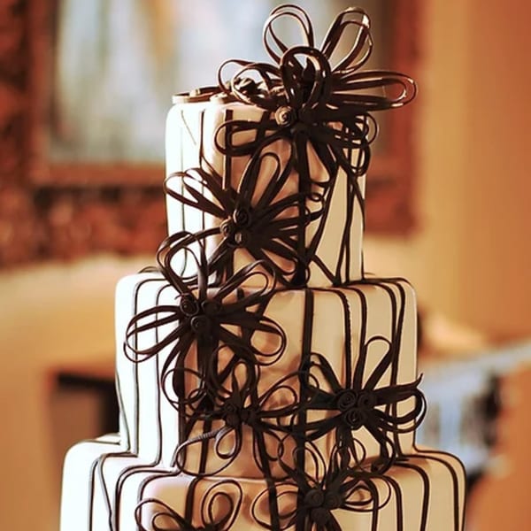 A multi-tiered white cake with intricate dark chocolate ribbon and bow decorations.
