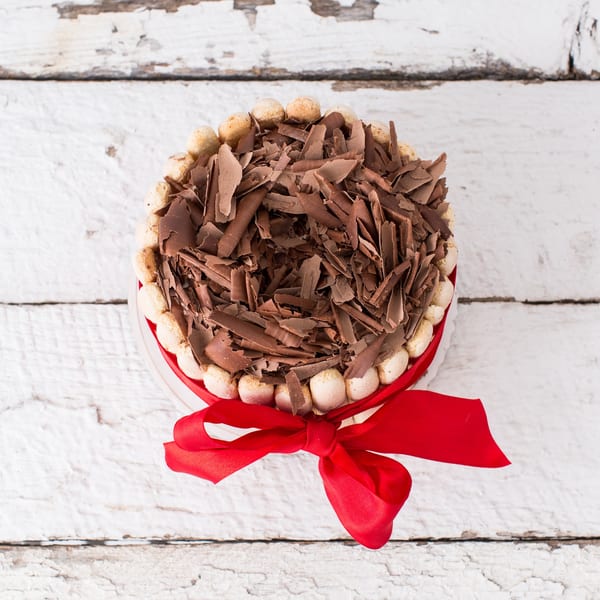 Overhead view of a tiramisu cake with chocolate shavings and ladyfingers, tied with a red ribbon.