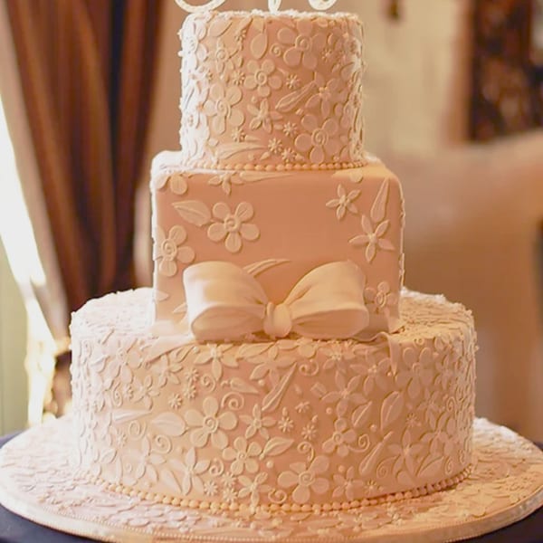A three-tiered wedding cake from Honeymoon Sweets, adorned with delicate white floral icing and a bow.