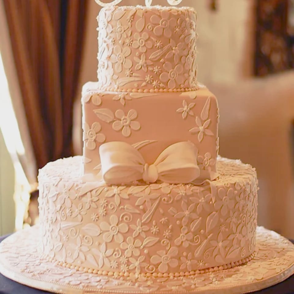A three-tiered wedding cake from Honeymoon Sweets, adorned with delicate white floral icing and a bow.