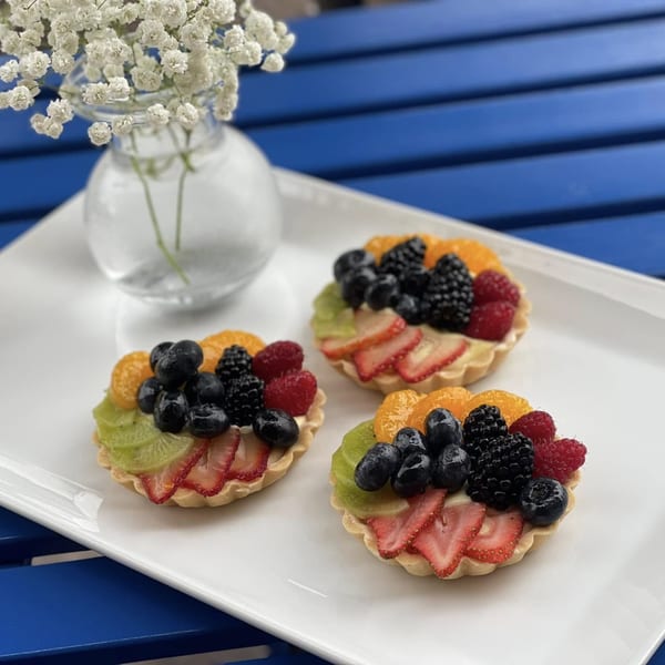 Three colorful fruit tarts with berries, kiwi, and oranges on a white platter with baby's breath.