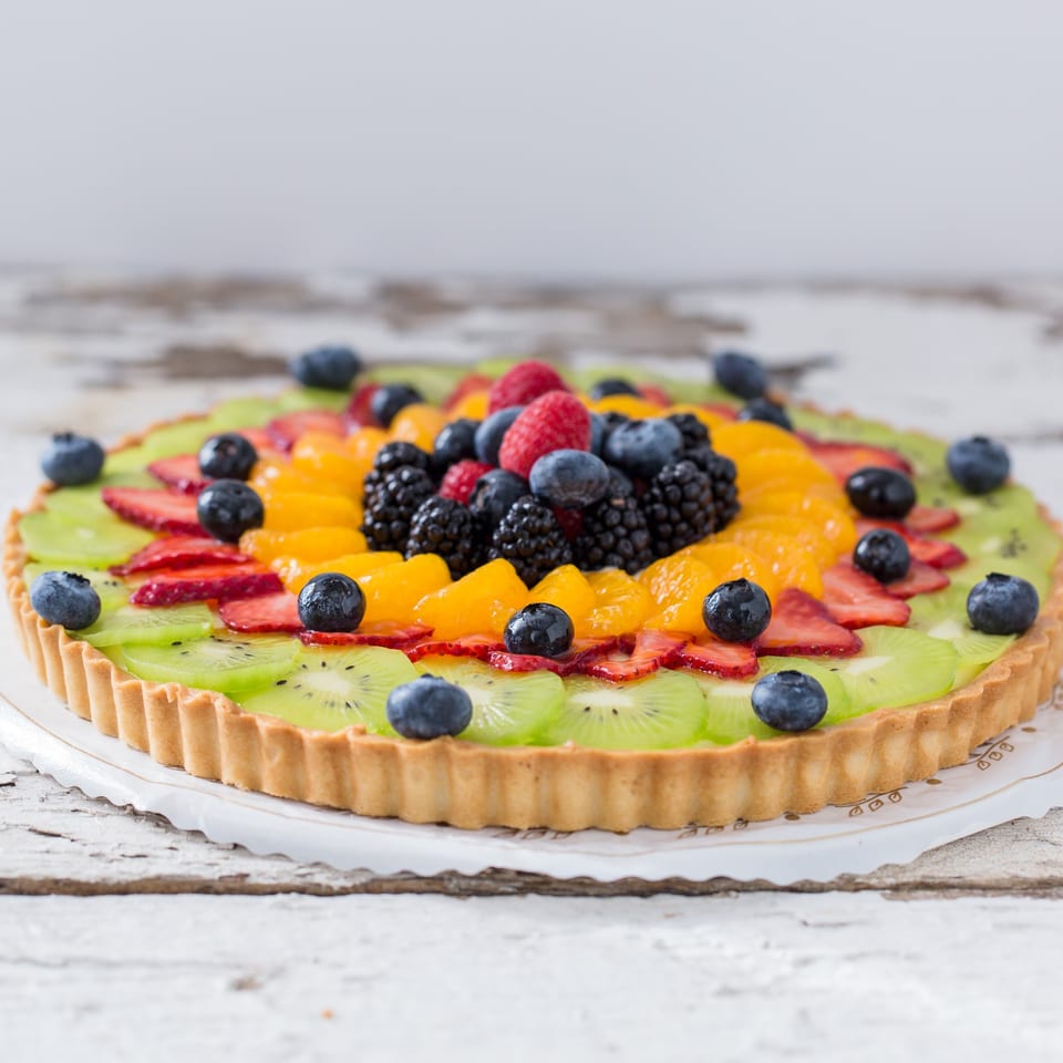 A vibrant fruit tart from Honeymoon Sweets, topped with kiwi, strawberries, blueberries, raspberries, and mandarins.