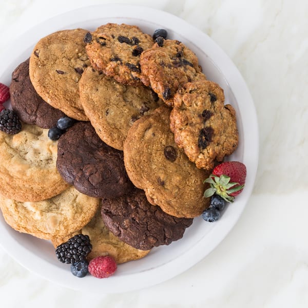 A white plate piled high with assorted cookies and fresh berries on a marble surface.