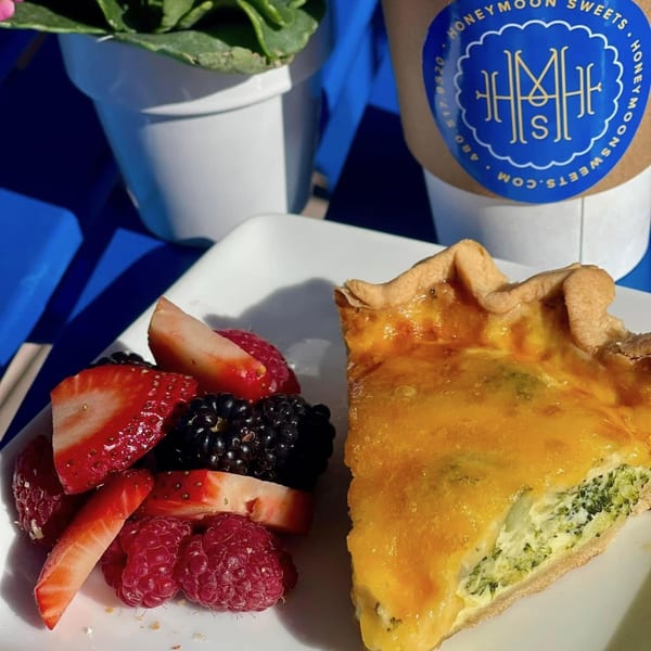A slice of quiche with a side of fresh berries and a Honeymoon Sweets coffee cup.