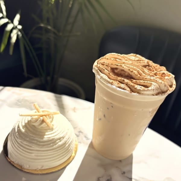 A white domed cake with wafer sticks and an iced coffee with whipped cream on a marble table.