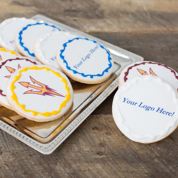 Custom logo cookies with white icing and colorful borders on a silver tray and wooden surface.