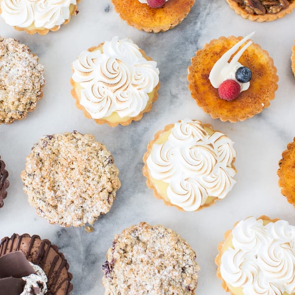 An overhead view of various Honeymoon Sweets European Bakery tarts, including meringue, fruit, and crumble.