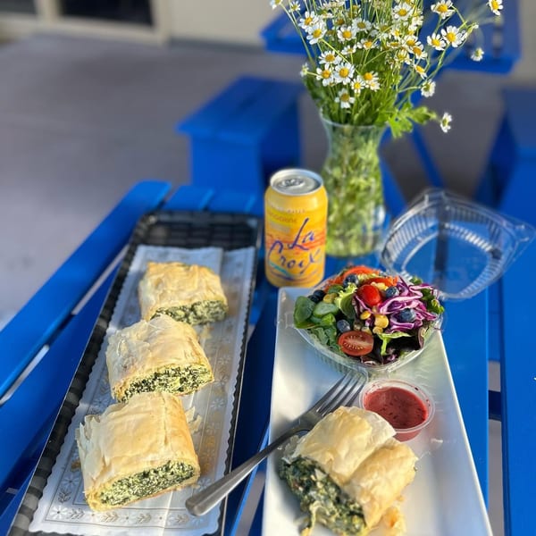 Spinach pies, a side salad, and a La Croix drink on a blue outdoor table with daisies.