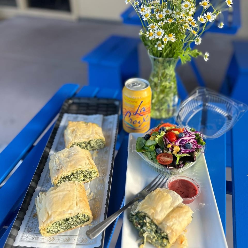 Spinach pies, a side salad, and a La Croix drink on a blue outdoor table with daisies.