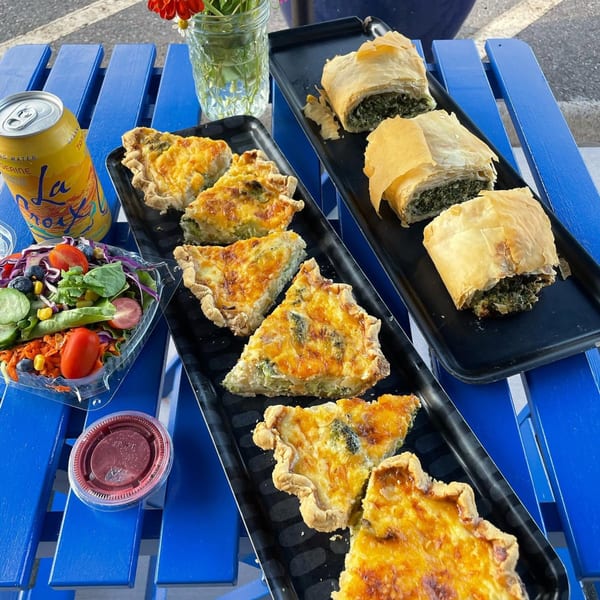 Quiche slices, spinach pastries, a side salad, and a La Croix can on a blue picnic table.