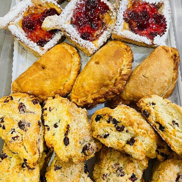 A tray of pastries including cherry danishes, golden empanadas, and cranberry scones.