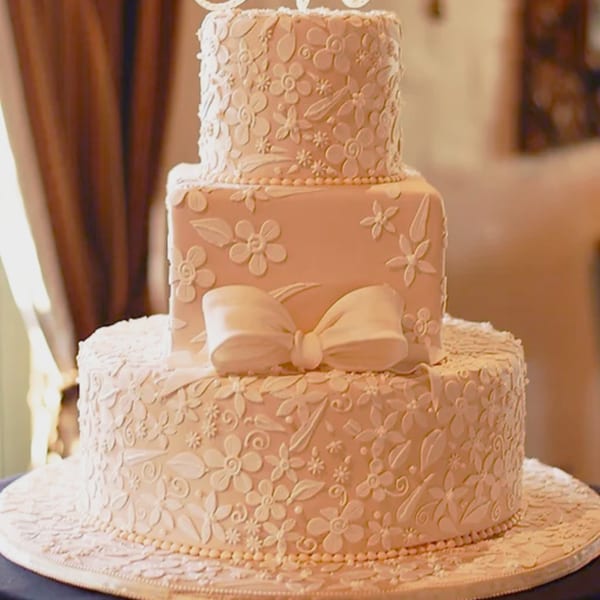 Three-tiered wedding cake from Honeymoon Sweets, adorned with delicate white floral icing and a large bow.