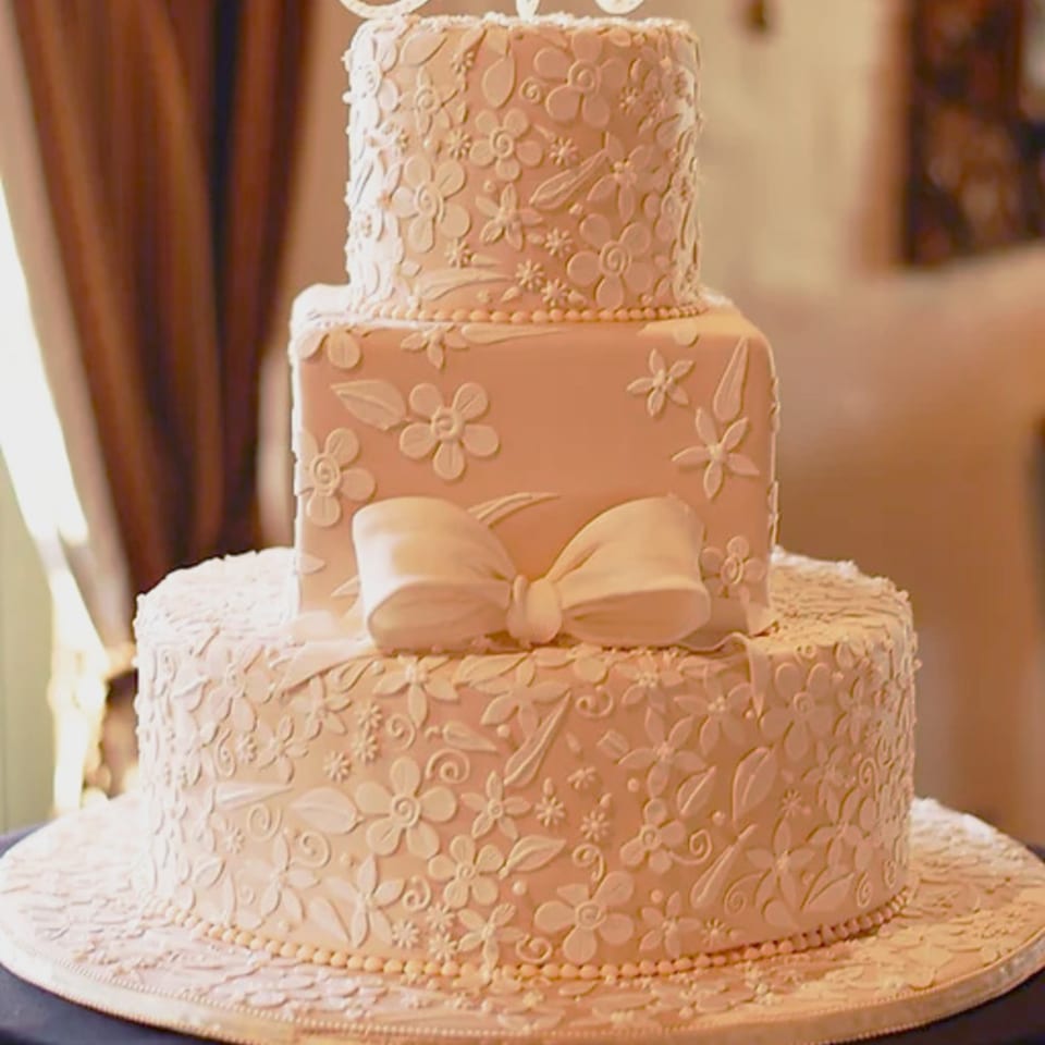 Three-tiered wedding cake from Honeymoon Sweets, adorned with delicate white floral icing and a large bow.