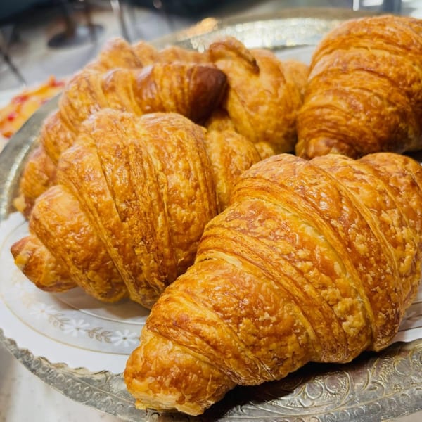 Golden-brown, flaky croissants piled on a decorative silver tray, ready to be served.