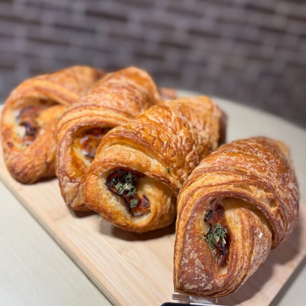 Four golden-brown savory croissants with visible herb filling, arranged on a light wooden board.