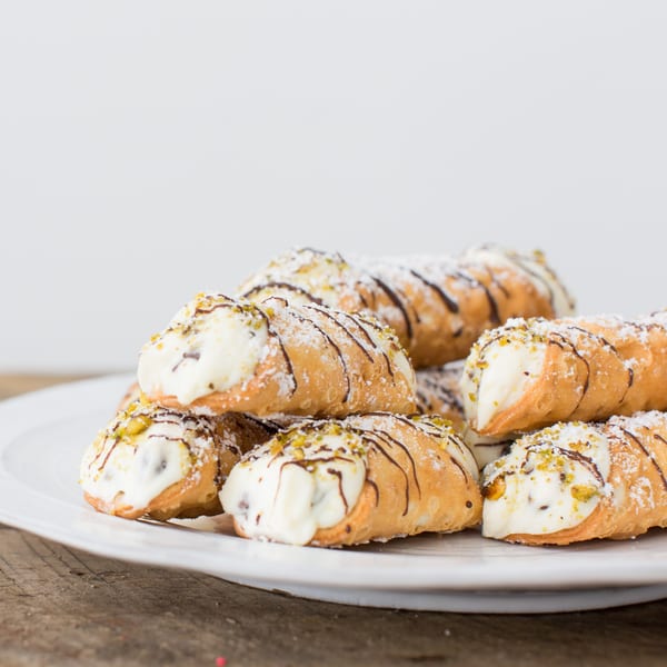 Honeymoon Sweets European Bakery cannolis, drizzled with chocolate, powdered sugar, and pistachios on a white plate.