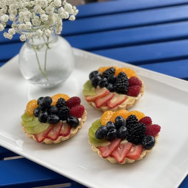 Three vibrant fruit tarts with berries, kiwi, and mandarins on a white platter with baby's breath.