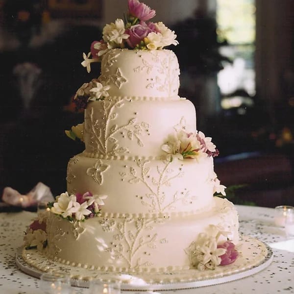 A five-tiered white wedding cake with intricate piping, silver beads, and pink and white flowers.